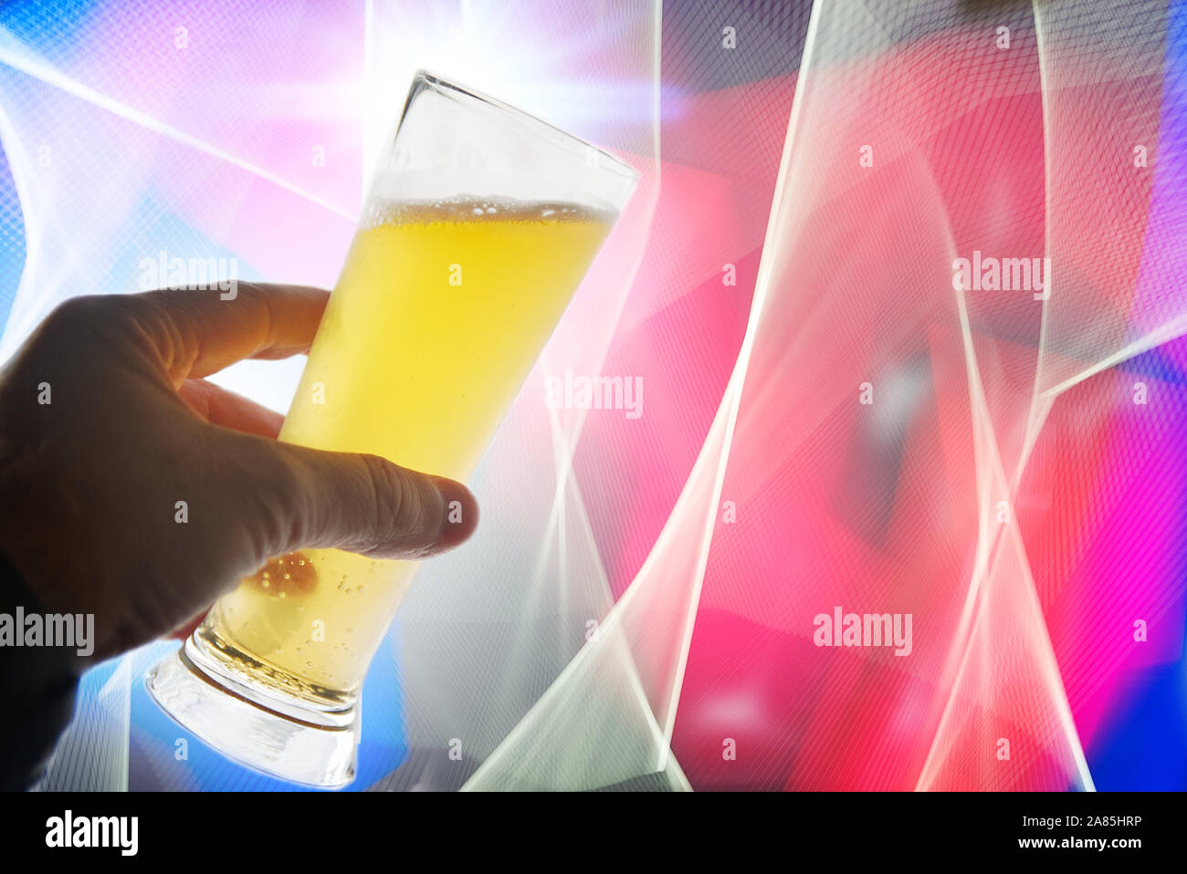 Man's hand holding a glass of beer against an abstract light background in a night club. Alcoholism and alcohol abuse concept with empty copy space Stock Photo