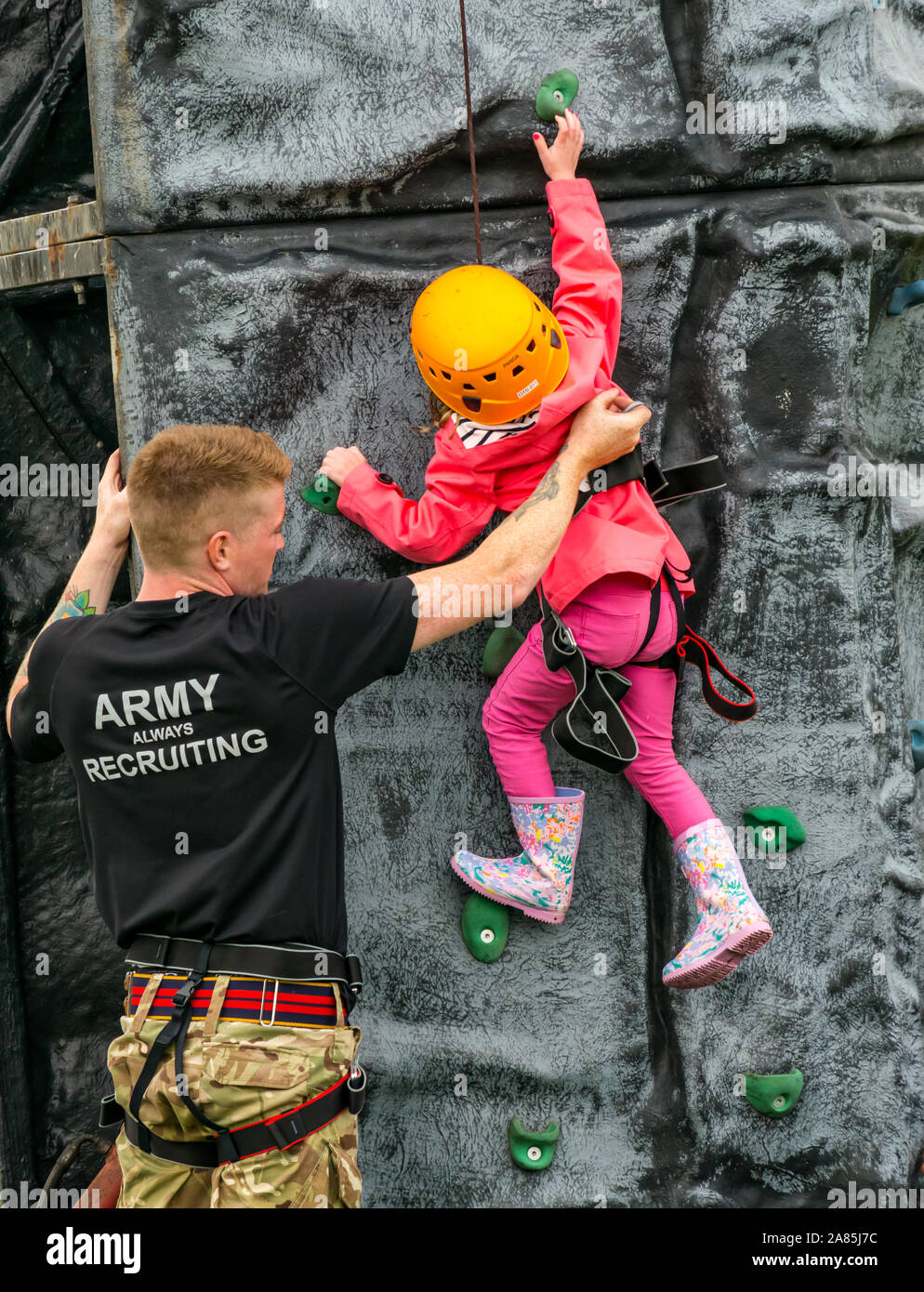 Army soldier helps a young child climb on a climbing wall, National airshow, East Fortune, East Lothian, Scotland, UK Stock Photo