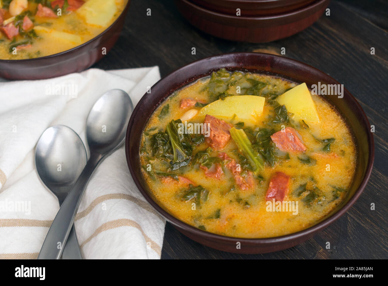 Portuguese Caldo Verde Soup: Bowls of traditional Portuguese sausage, potato, and kale soup on a dark wood background Stock Photo