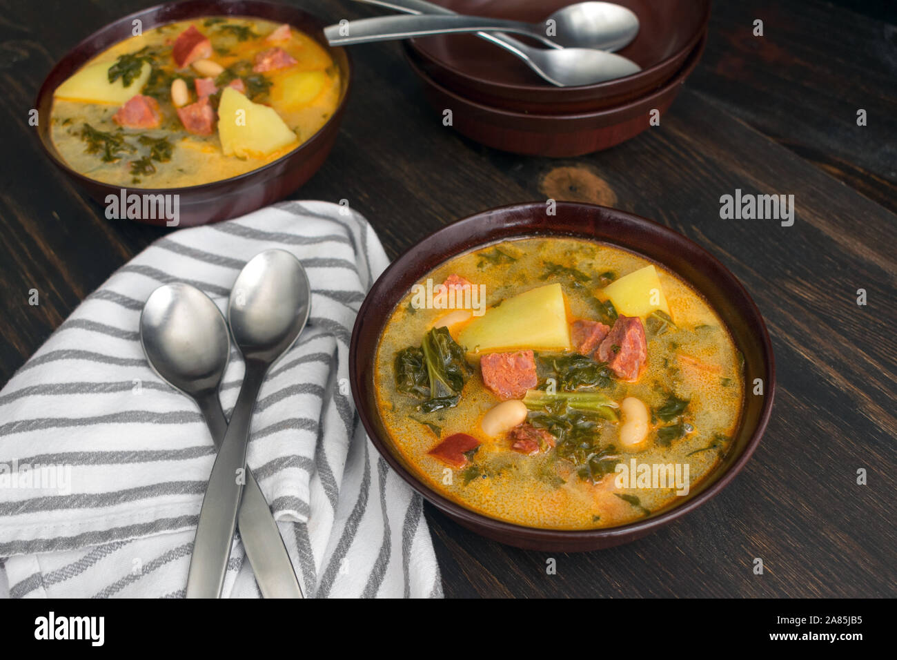 Portuguese Caldo Verde Soup: Bowls of traditional Portuguese sausage, potato, and kale soup on a dark wood background Stock Photo