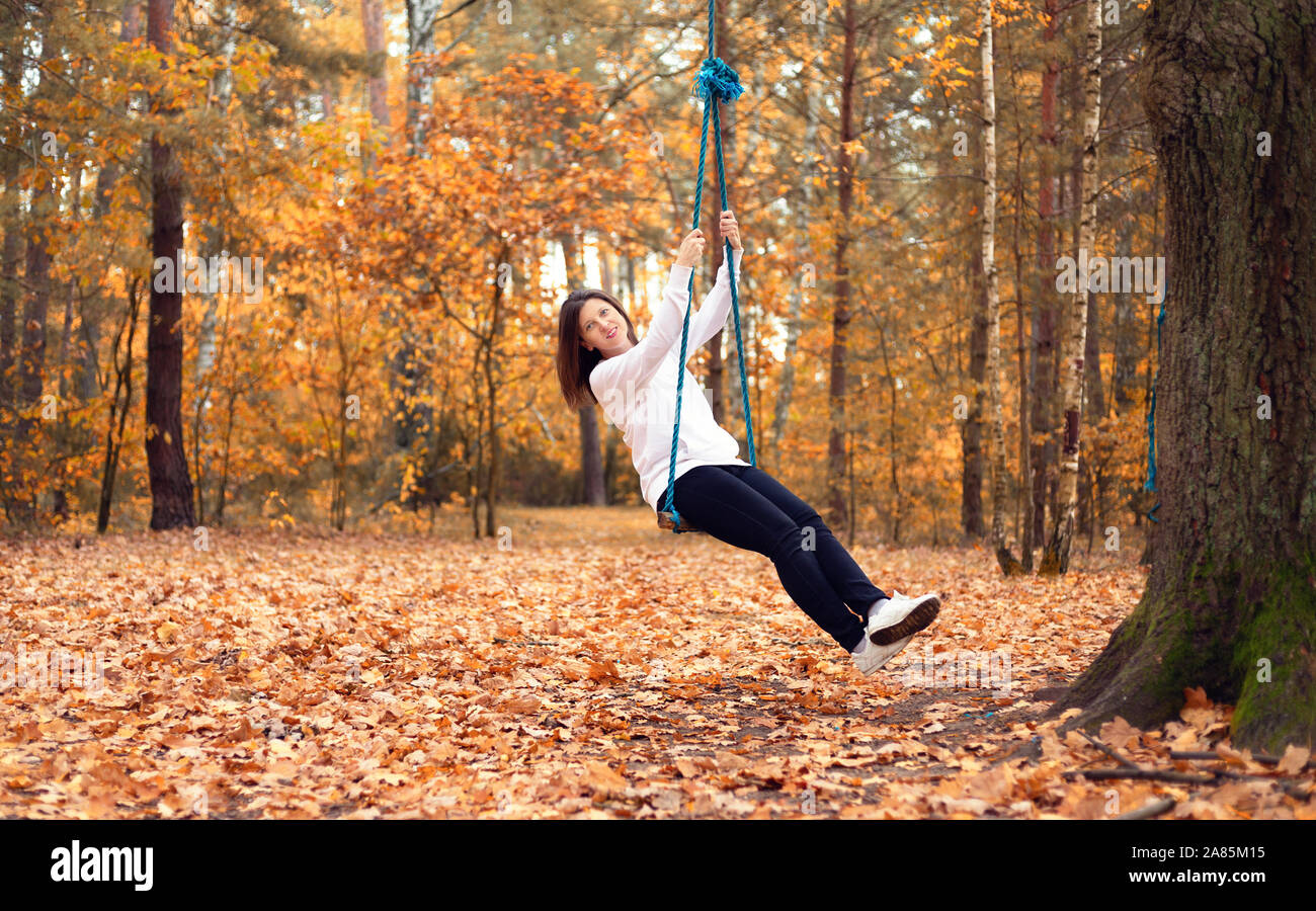 Happy woman on a swing in the autumn forest Stock Photo