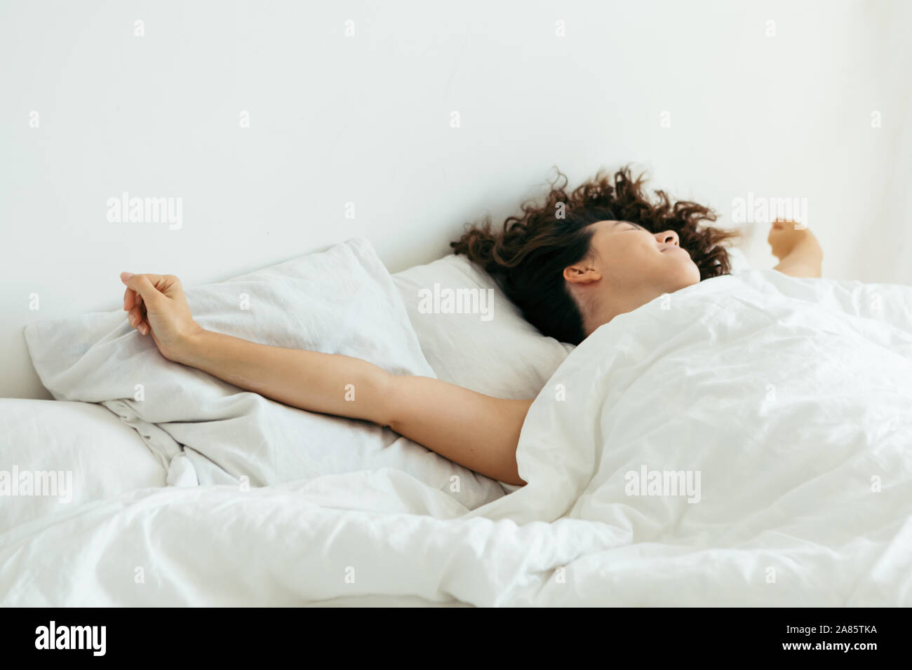 young pretty woman in bed with white sheets bright light Stock Photo
