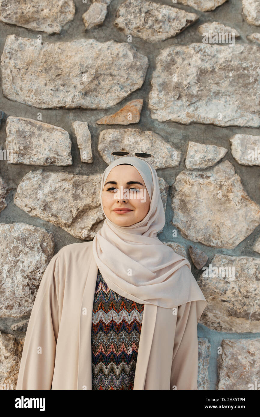 portrait of young European Muslim women with hijab. Stone wall is ...