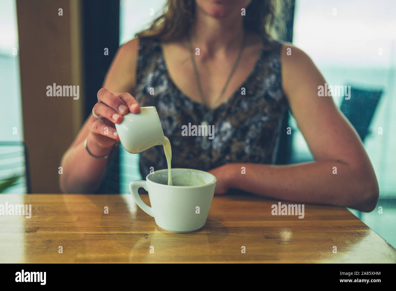 A young woman is pouring cream in her coffee in a cafe Stock Photo