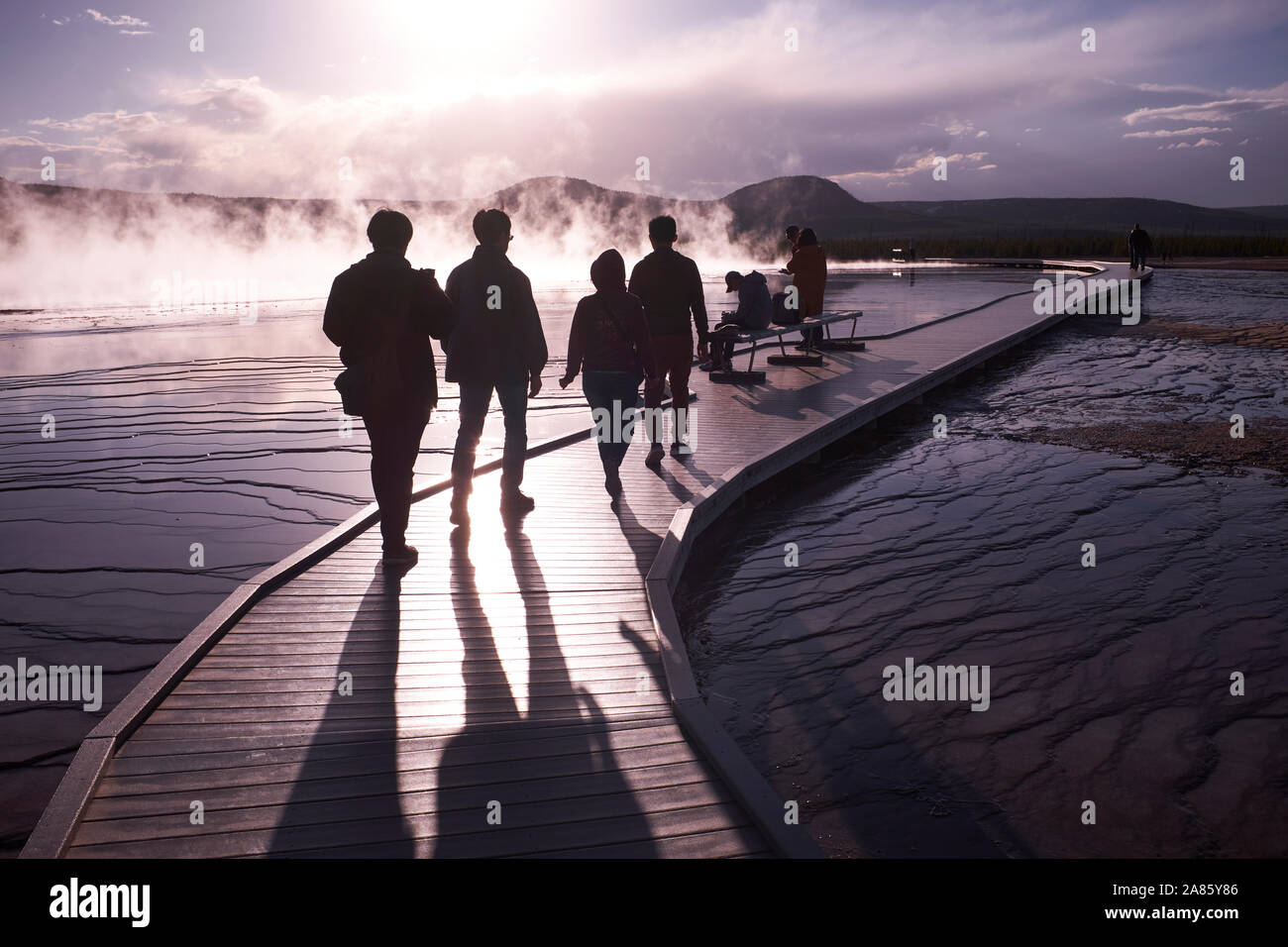 Visitors are silhouetted against the sun and rising steam at Grand Prismatic Hot Springs in Yellowstone National Park, Wyoming, USA Stock Photo