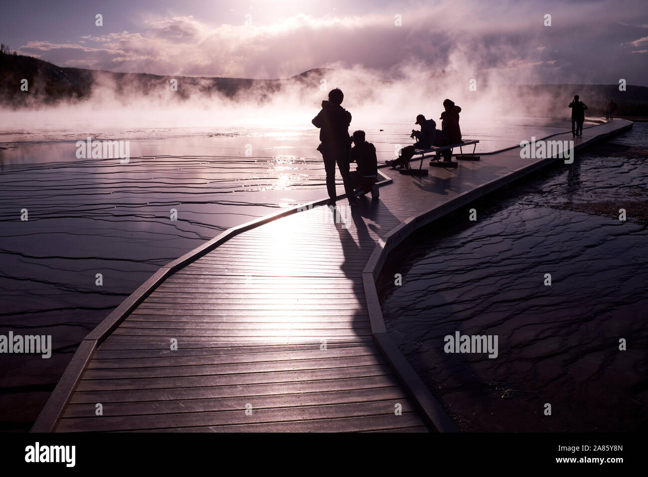 Visitors are silhouetted against the sun and rising steam at Grand Prismatic Hot Springs in Yellowstone National Park, Wyoming, USA Stock Photo