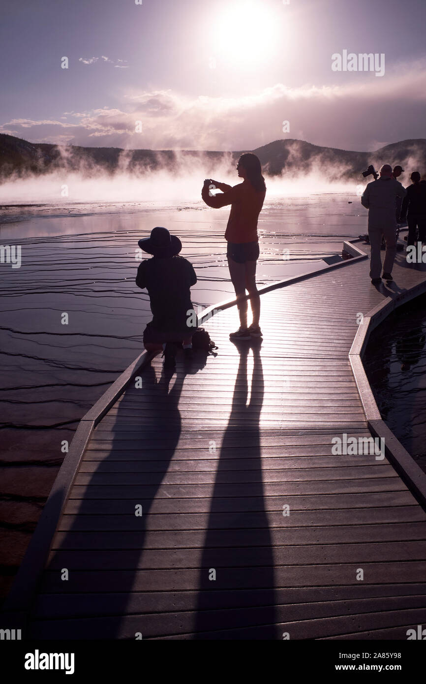 Visitors are silhouetted against the sun and rising steam at Grand Prismatic Hot Springs in Yellowstone National Park, Wyoming, USA Stock Photo