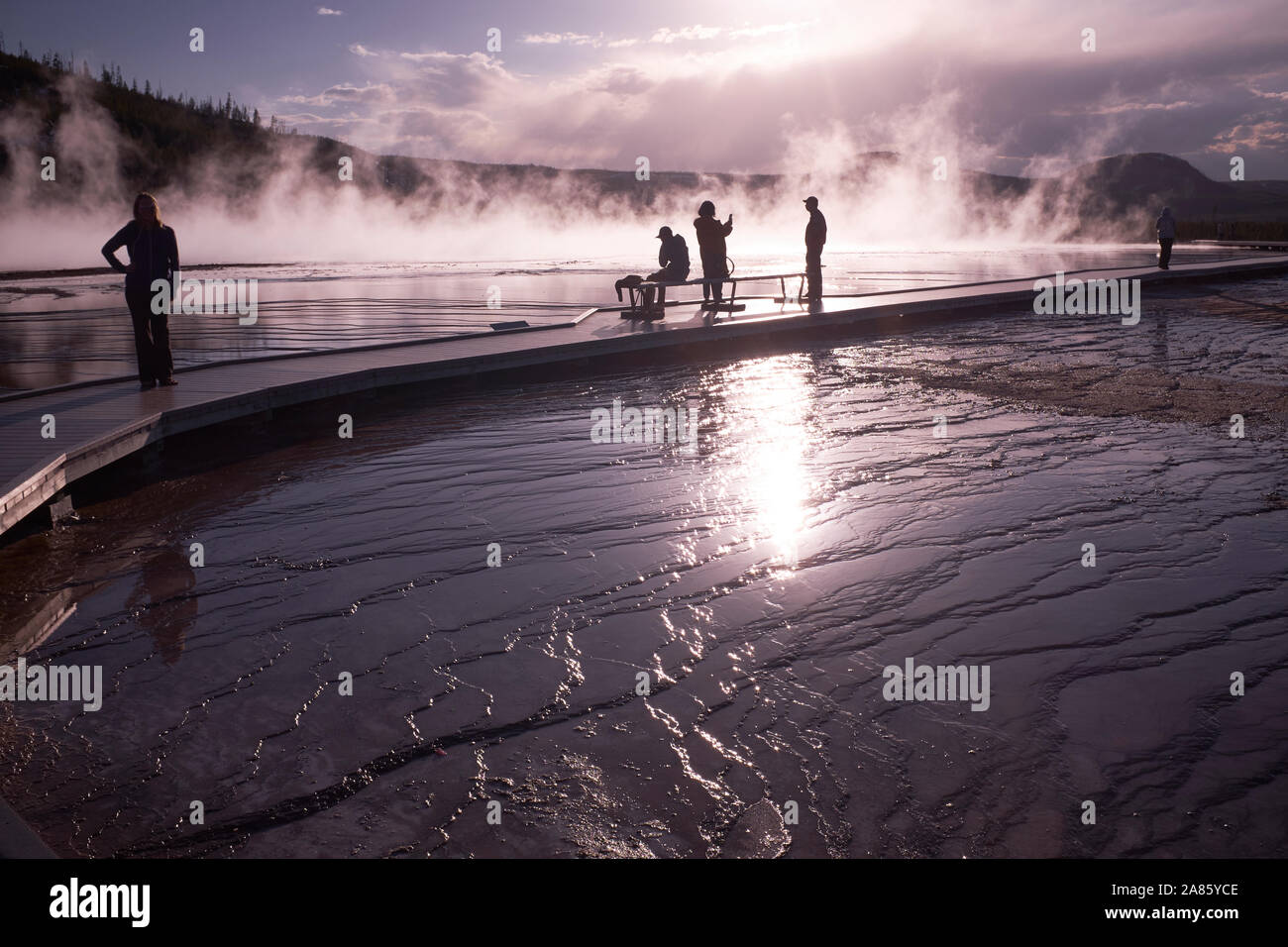 Visitors are silhouetted against the sun and rising steam at Grand Prismatic Hot Springs in Yellowstone National Park, Wyoming, USA Stock Photo