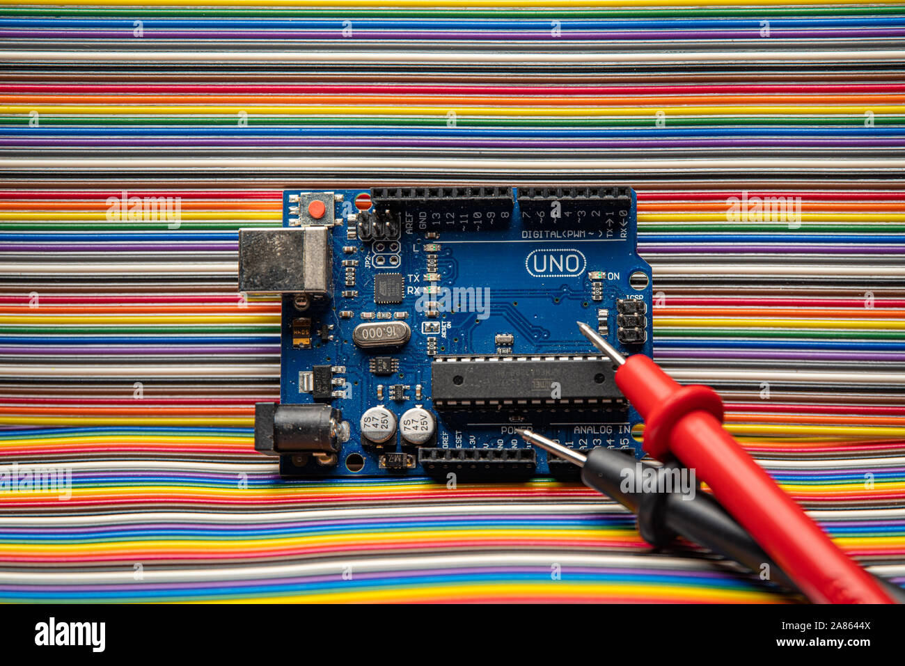 Arduino Uno displayed on jumper wire background with meter probes. Stock Photo