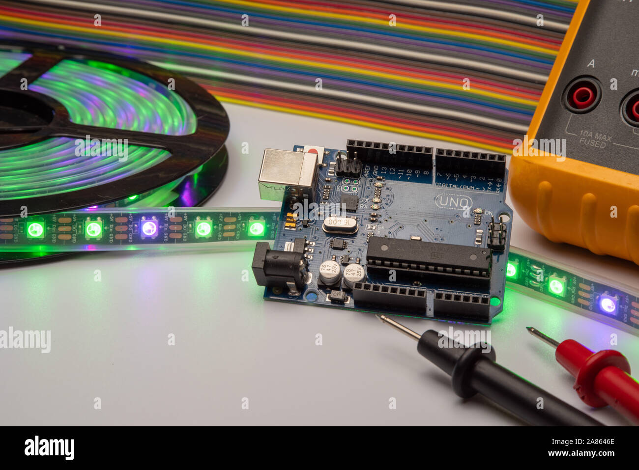 Arduino Uno displayed with LED strip, multimeter, and jumper wire background. Stock Photo