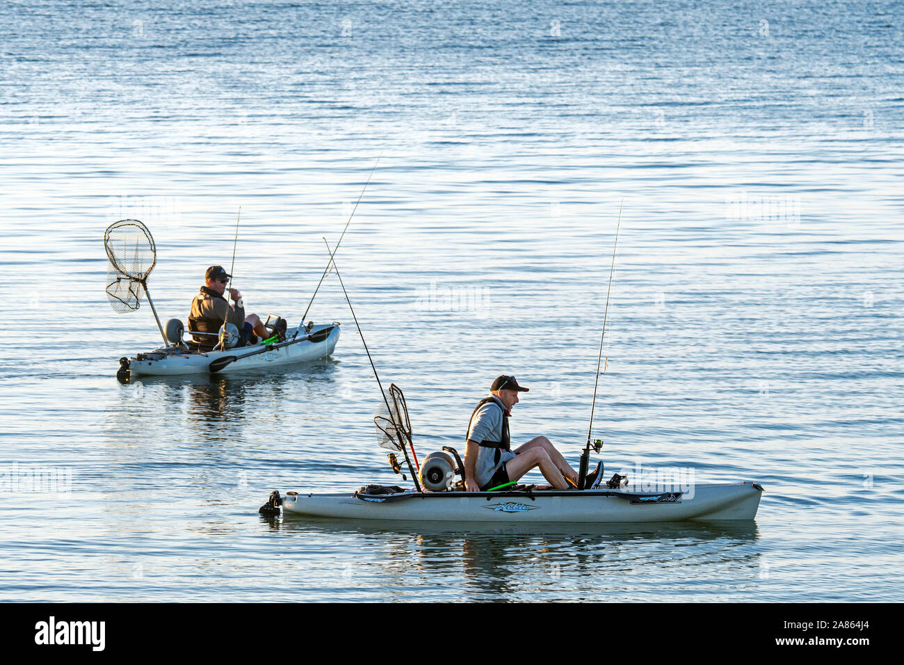 Two sea anglers fishing from pedal drive kayaks / pedal driven kayak at sunset Stock Photo