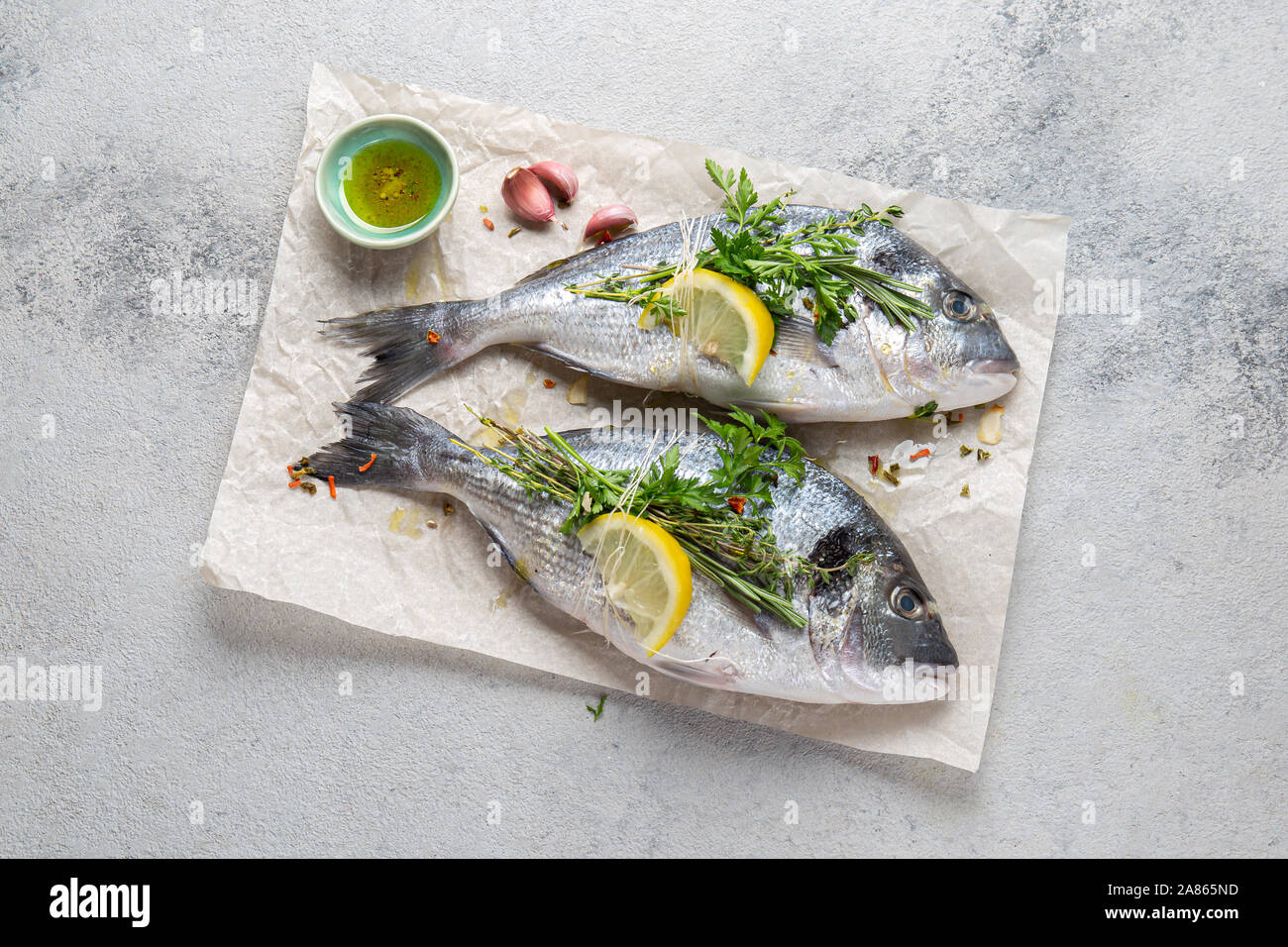 Dorada fish, raw fresh sea bream with lemon and herbs on a grey stone background, top view. Stock Photo