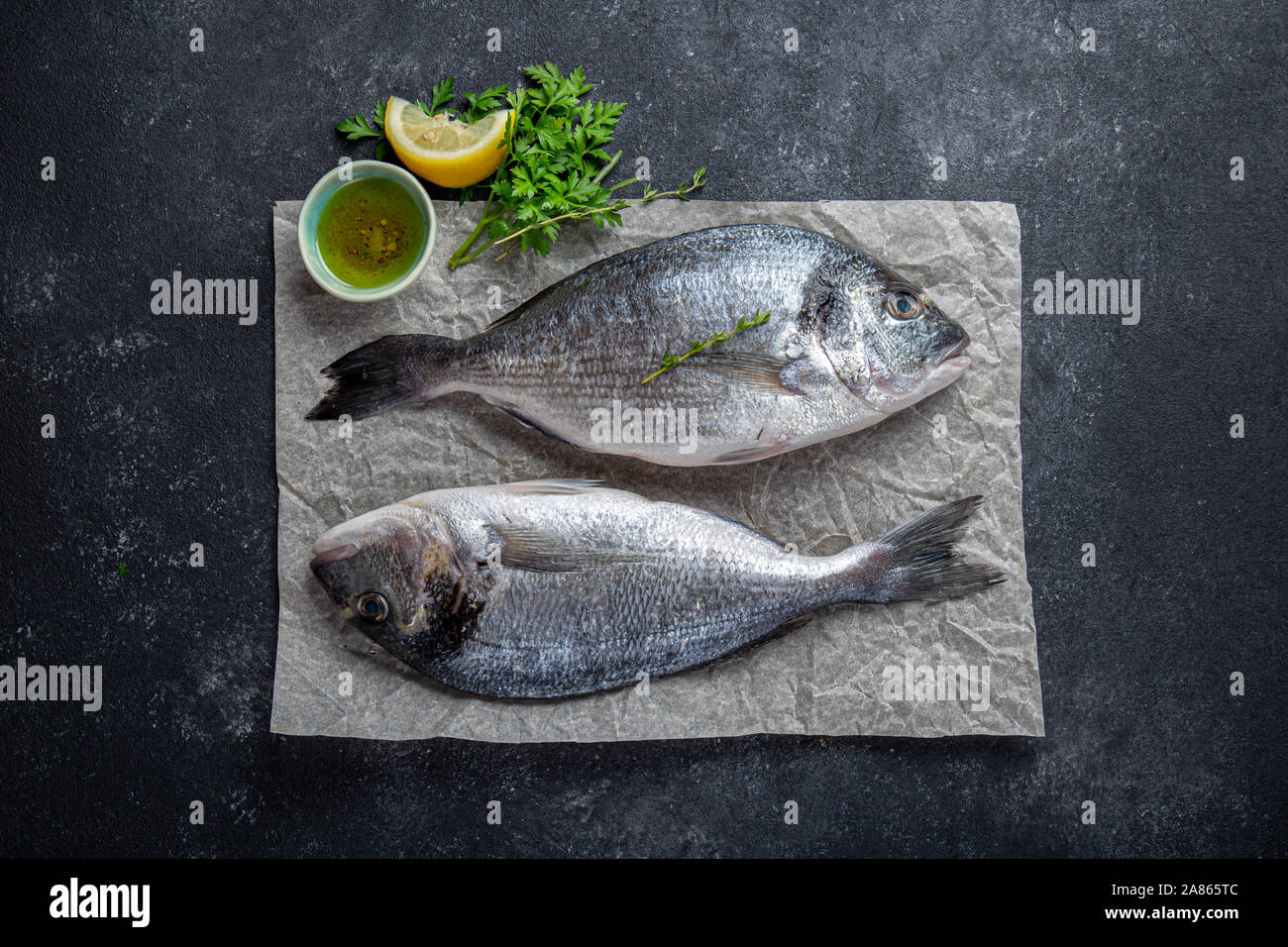 Dorada fish, raw fresh sea bream with lemon and herbs on a grey stone background, top view. Stock Photo