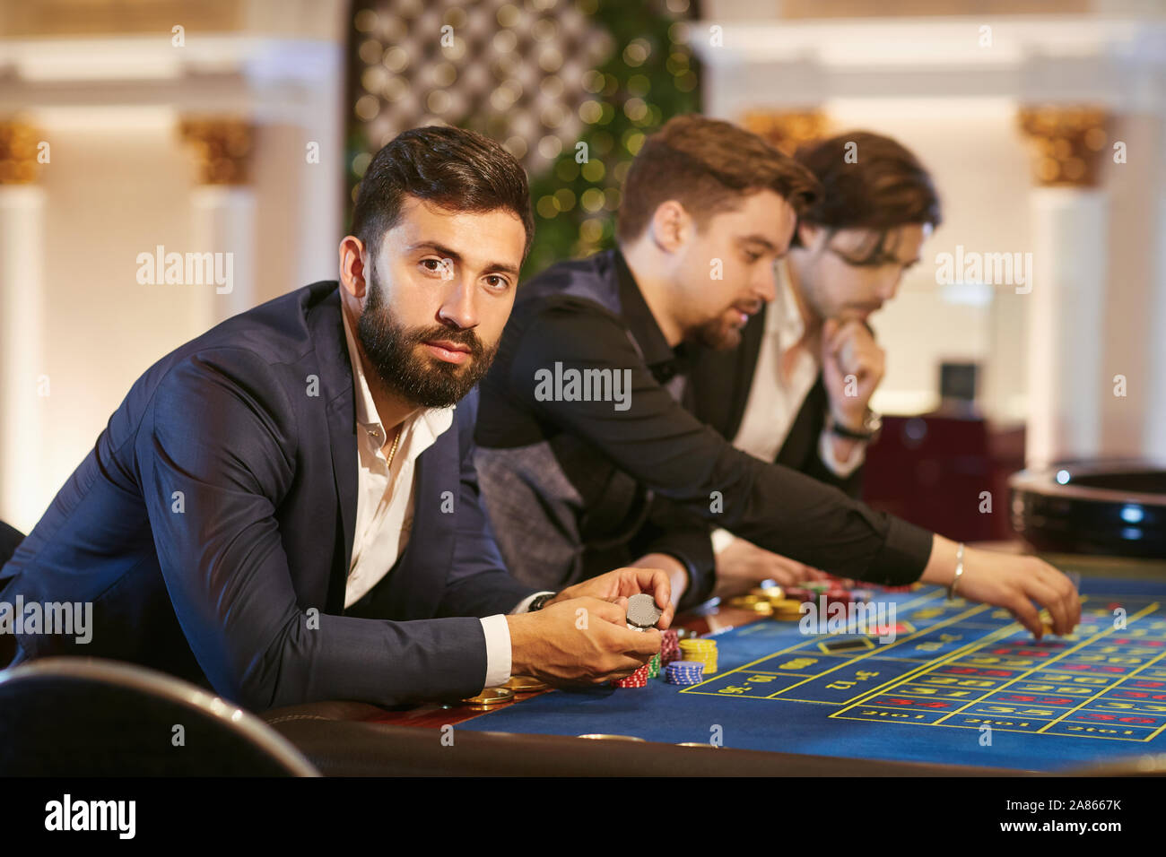 A man in a suit with a glass of whiskey sitting at table roulette playing poker at a casino. Stock Photo