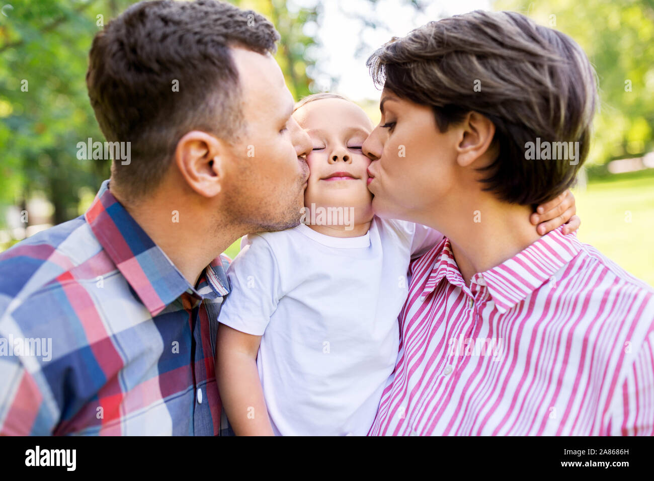 mother and father kissing their little son at park Stock Photo