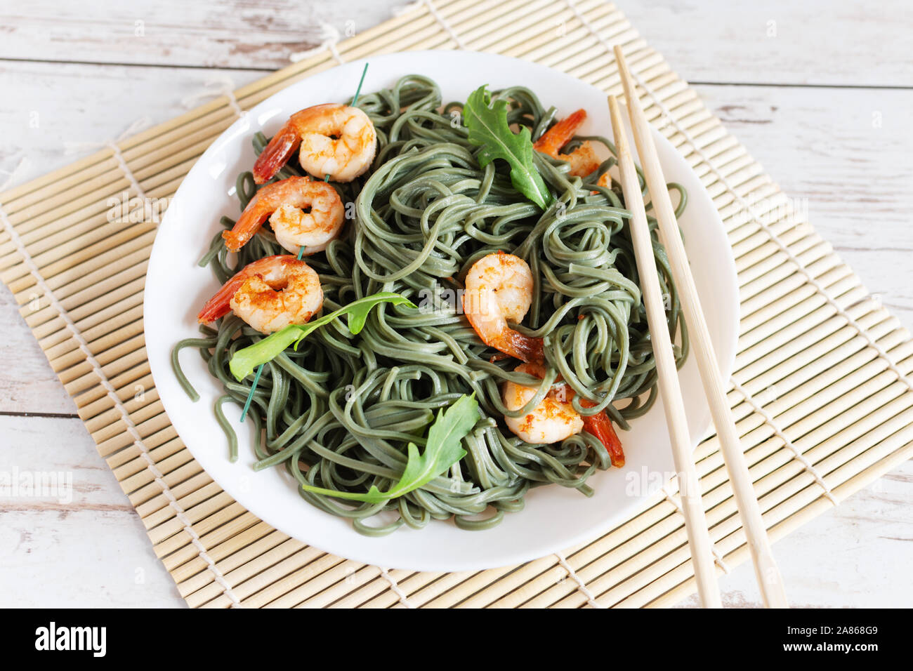Soba spirulina noodles with shrimps on a white plate top view. Asian food creative concept. Stock Photo