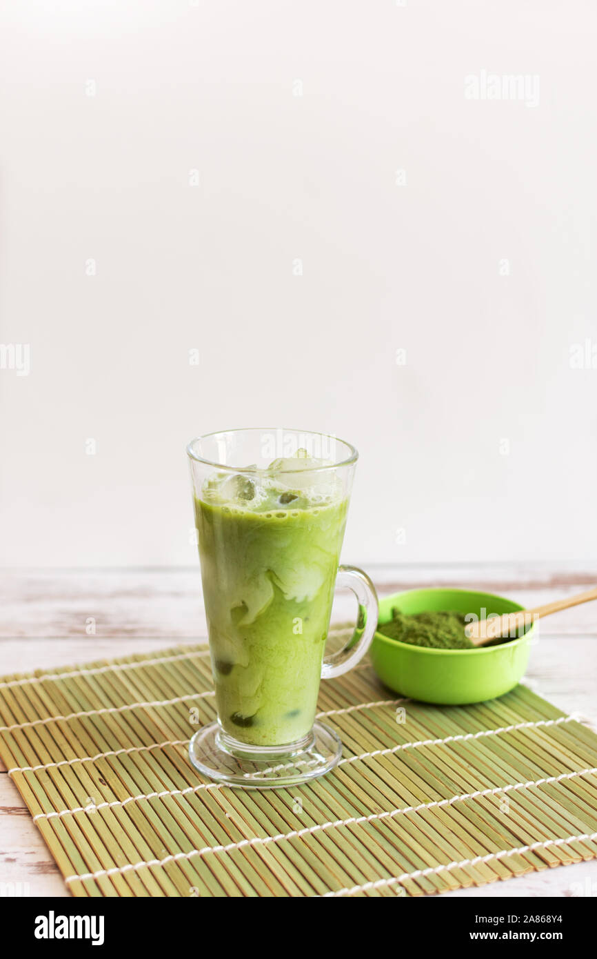 Iced matcha latte drink in tumbler glass with coconut milk pouring from pitcher by hand, copy space. Summer refreshing vegan beverage cold drink. Stock Photo