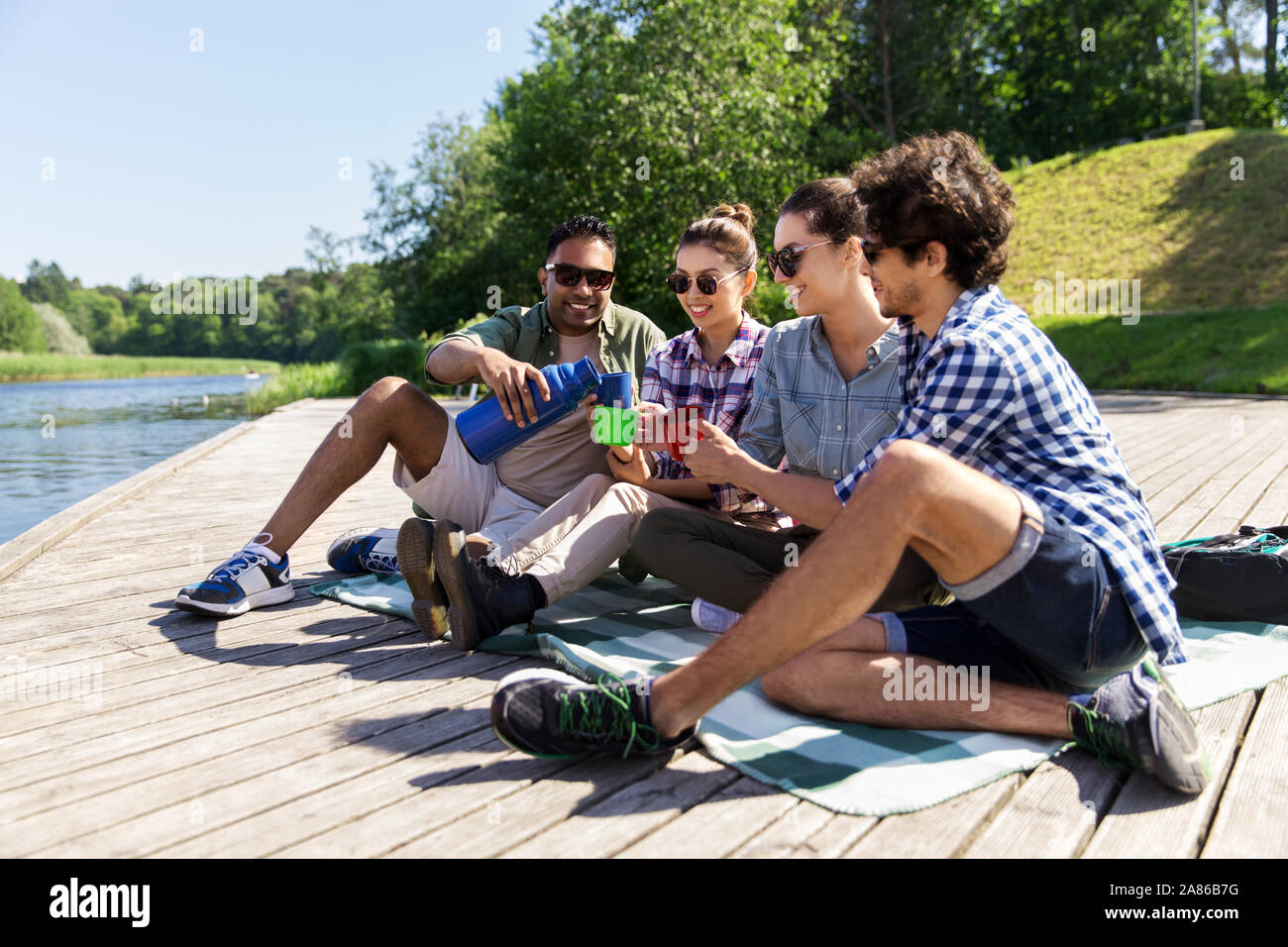 happy friends drinking tea from thermos in summer Stock Photo - Alamy