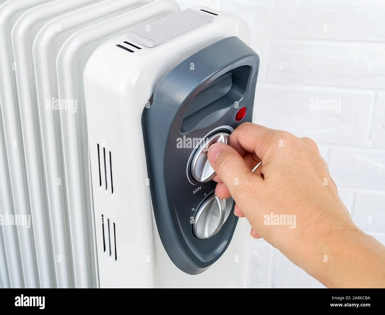 Woman hand turns on the thermostat knob of an electric oil heater. White oil-filled  radiator for home and office. House heating and comfort Stock Photo - Alamy