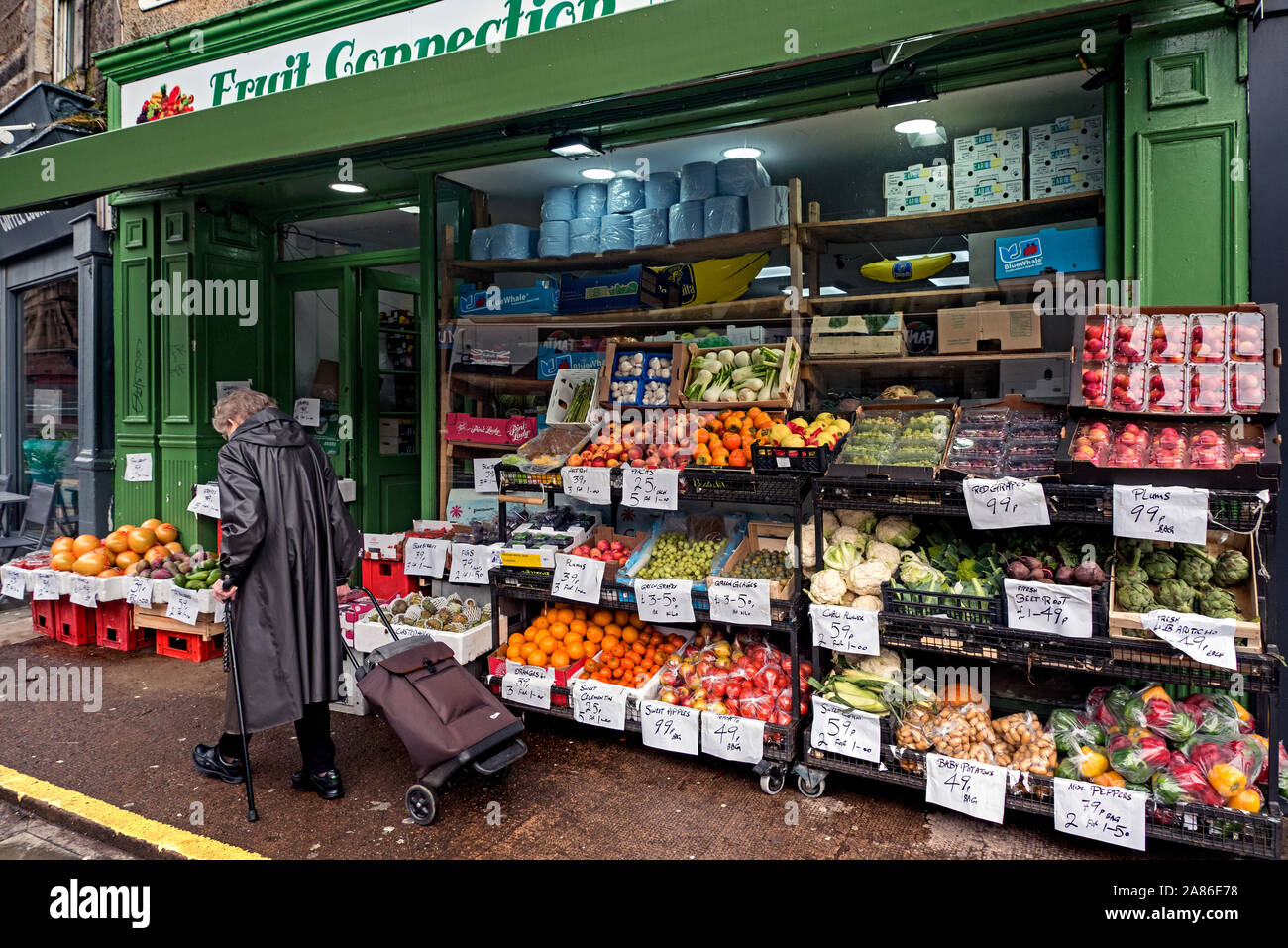 An elderly woman with her shopping trolley walks by a greengrocer's shop in Newington, Edinburgh, Scotland, UK. Stock Photo