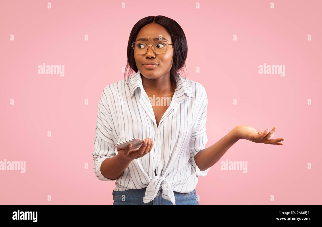 Irritated Girl Holding Smartphone Shrugging Shoulders On Pink Background Stock Photo