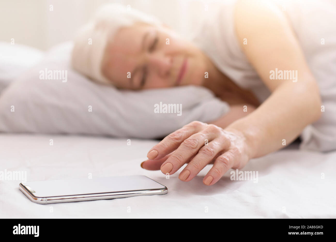 Senior woman waking up in her bed and checking her phone Stock Photo