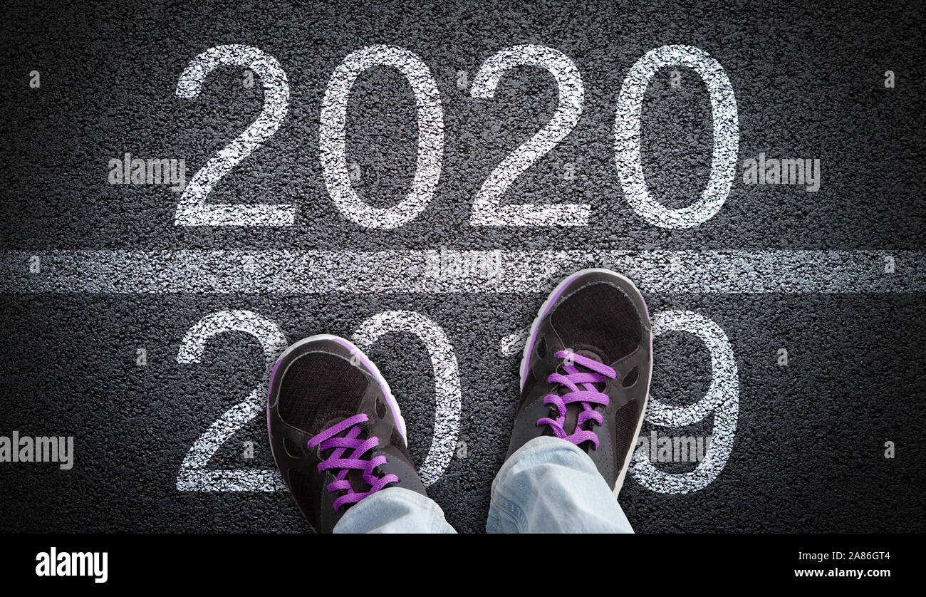A person in jeans and shoes walking on asphalt road from 2019 into New Year 2020. Concept of new beginning and directions, or stepping into a new year Stock Photo
