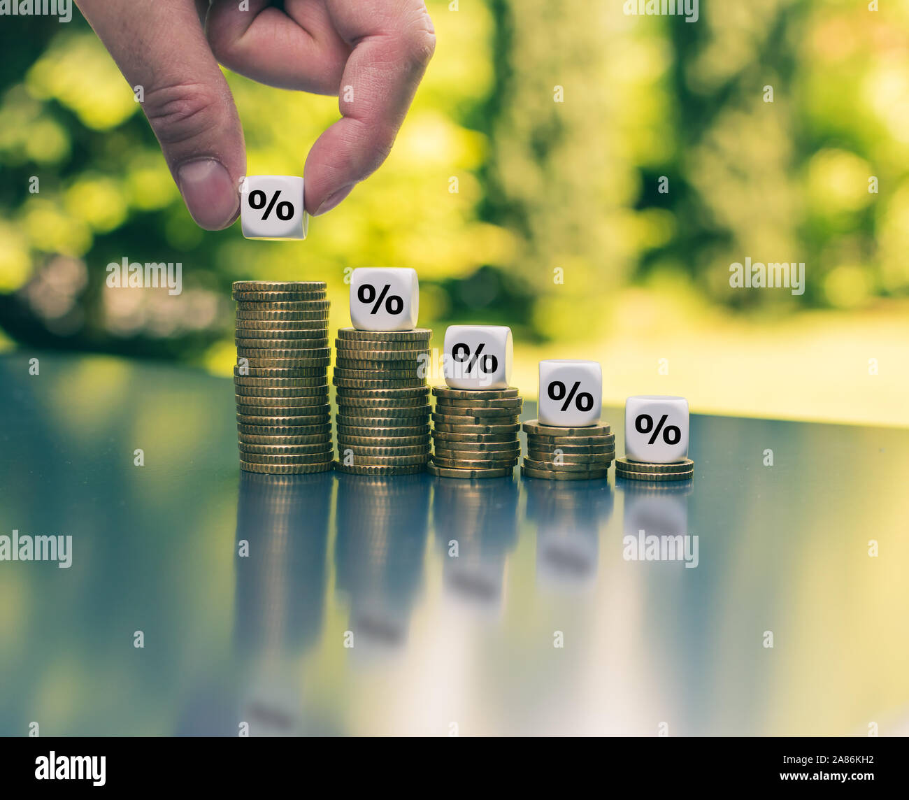 Dice with percentage symbols on decreasing high stacks of coins. Stock Photo