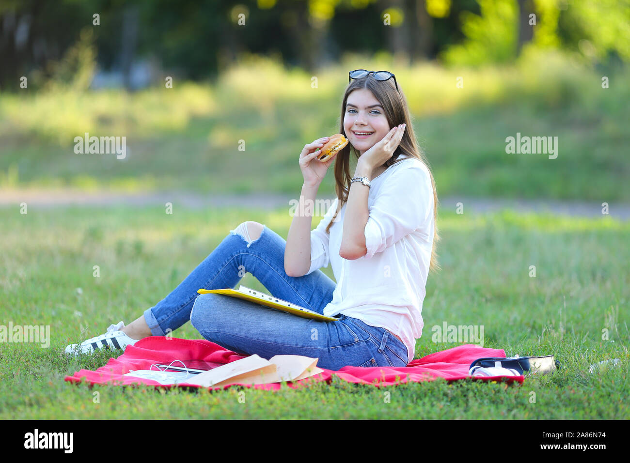 young girl sitting on the grass in the park and works at a laptop and ...
