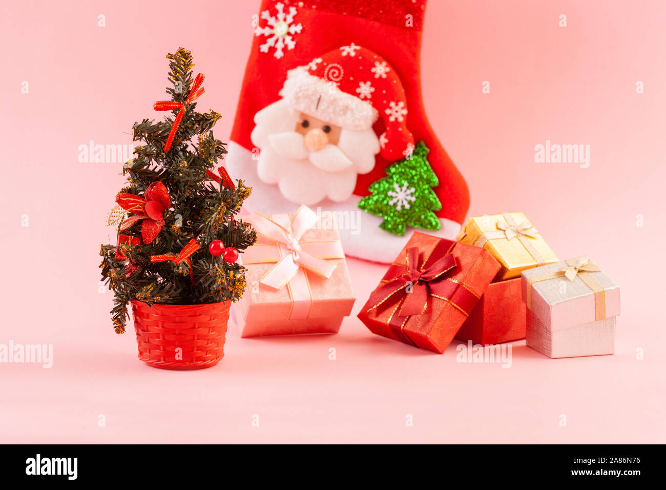 Christmas concept. Decorated Christmas tree with four gift boxes on a pink background. Gift sock in the background. Stock Photo