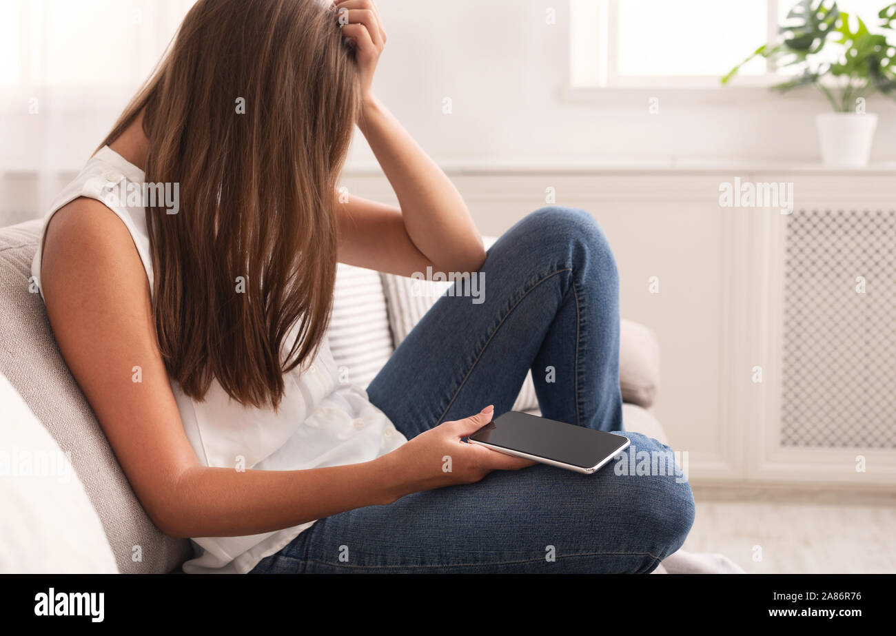 Depressed Girl Holding Phone Crying Sitting On Couch At Home Stock Photo