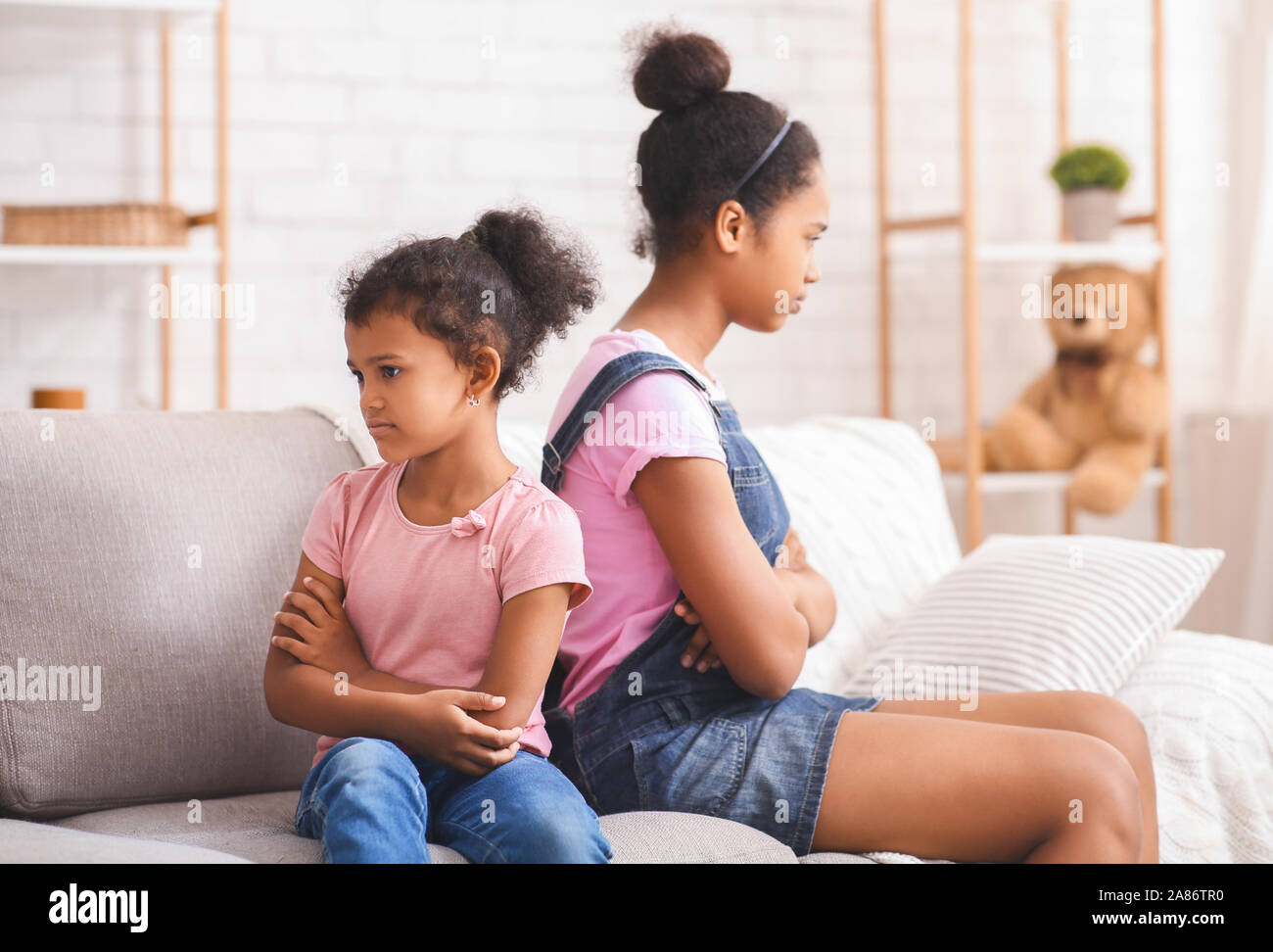 Grumpy african american sisters sitting back to back on couch Stock ...