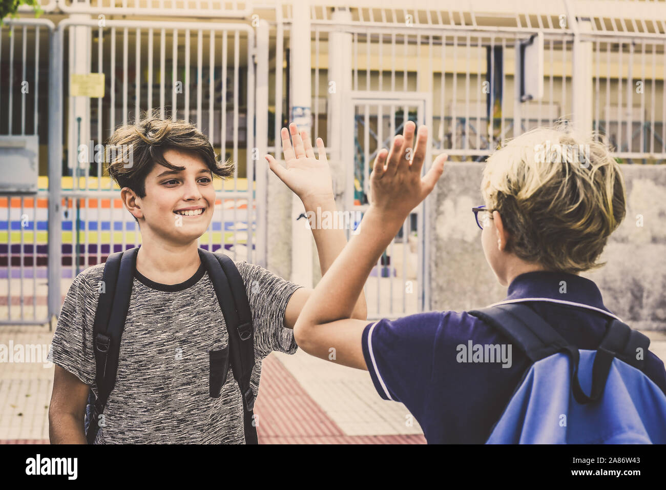 Two young students greet each other before the lessons. Happy boys with backpack meet out of institute after summer holidays the first day of school. Stock Photo