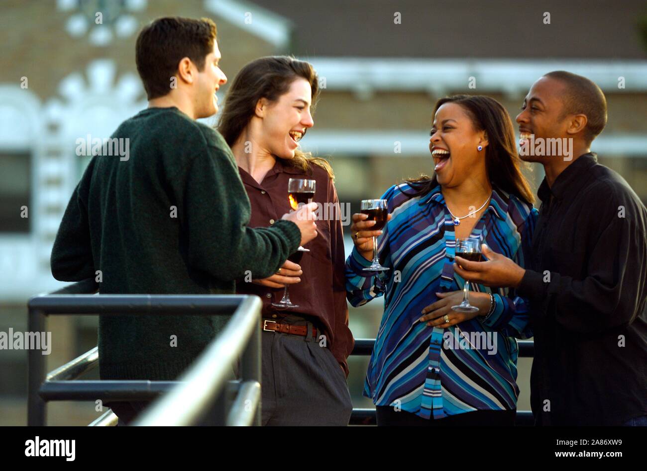 African-American and Caucasian couples enjoying cocktails on the roof deck Midsummer Stock Photo