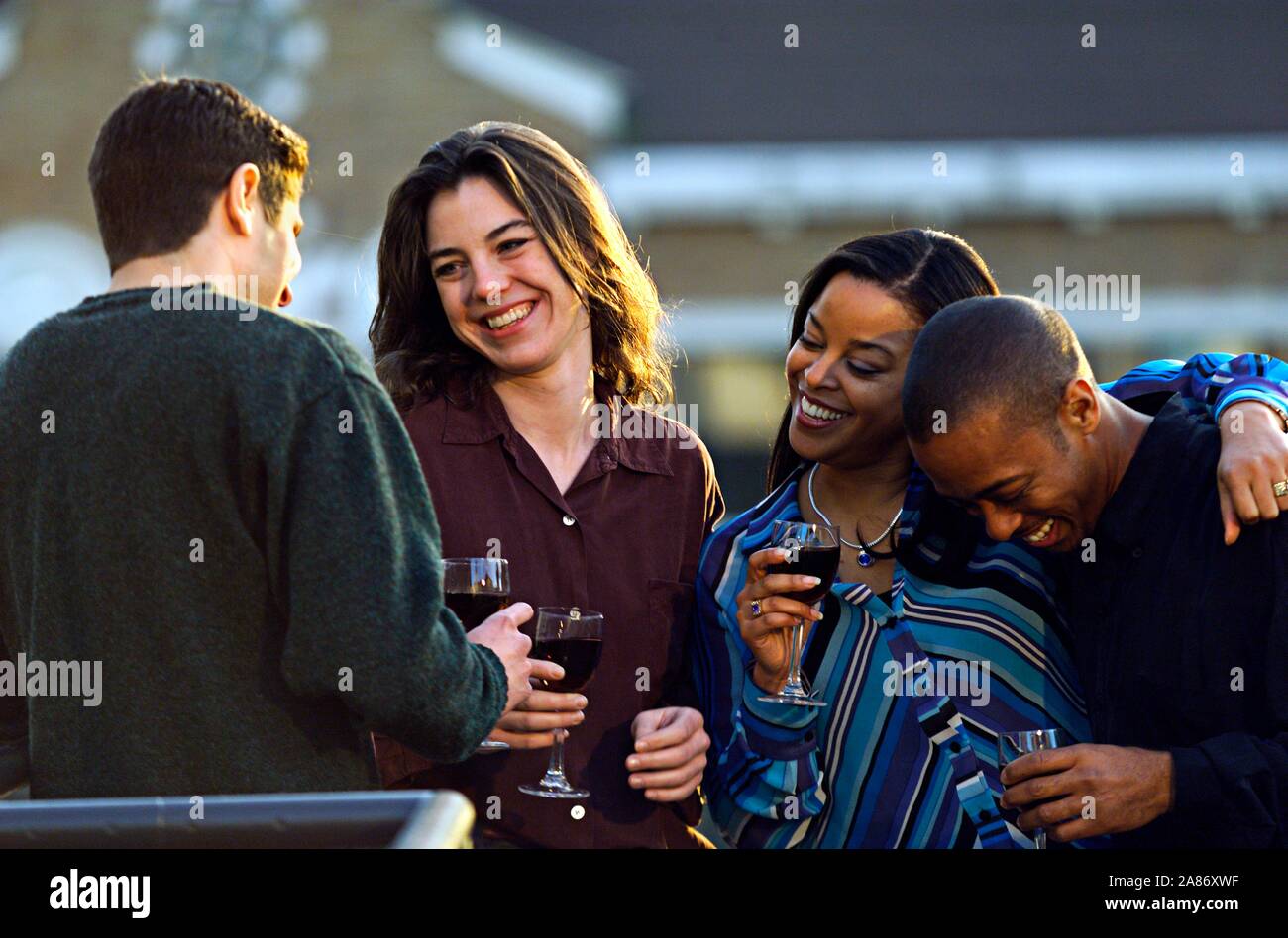 African-American and Caucasian couples enjoying cocktails on the roof deck Midsummer Stock Photo