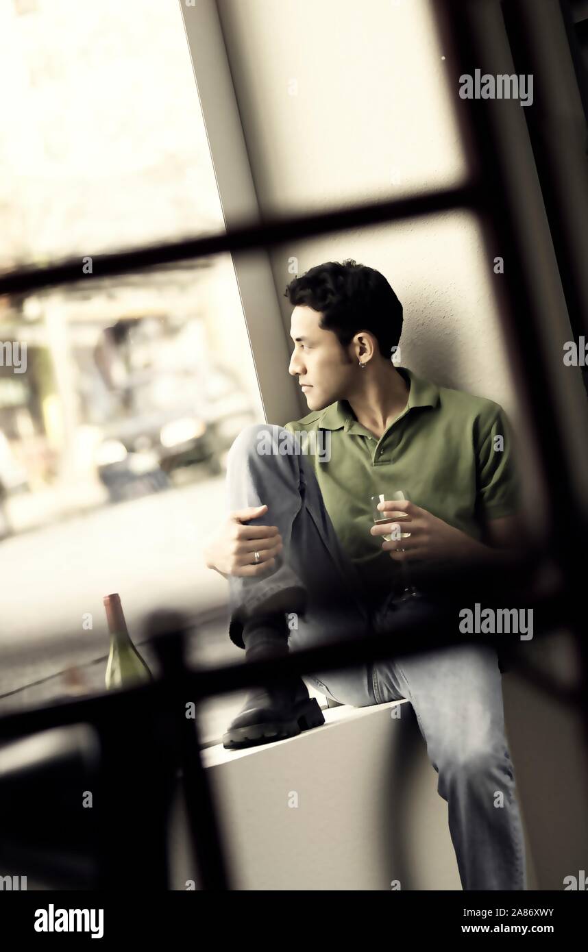 Asian man sitting alone in a large window with a glass of wine Stock Photo