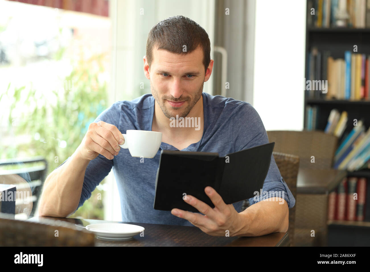 Front view portrait of a serious man reading an ebook sitting in a coffee shop Stock Photo