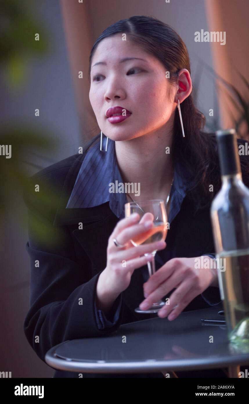 Attractive Asian woman sitting alone at a café table with a glass of ...