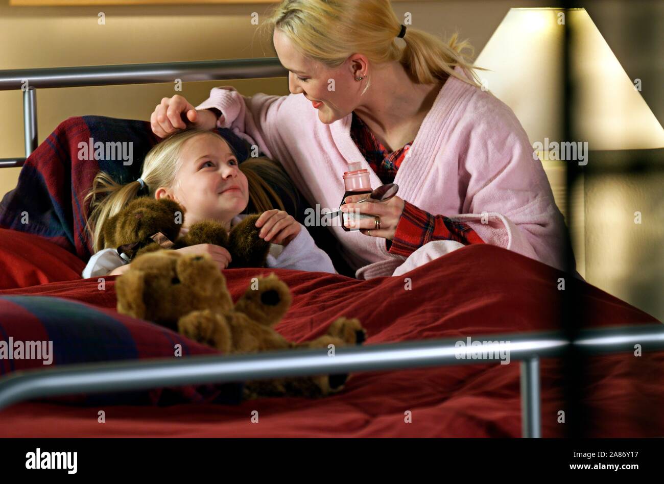 Little girl holding her teddy bear being comforted by her mother as she is recovering from a cold Stock Photo