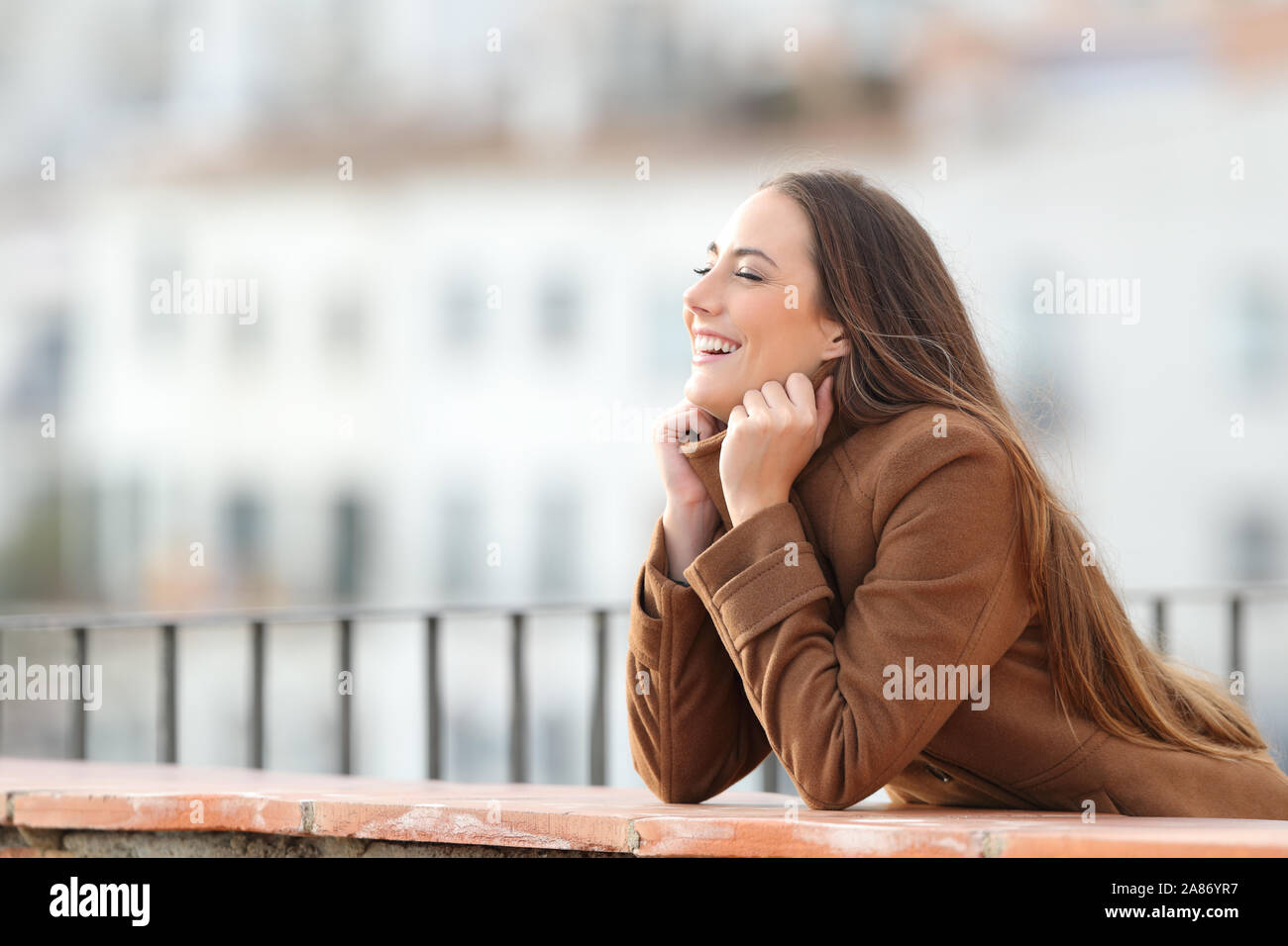 Happy woman heating grabbing jacket in a balcony in winter Stock Photo