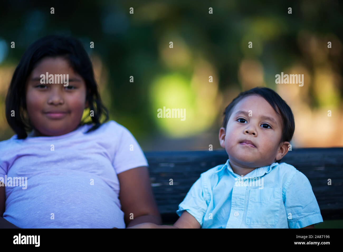 A little brother sitting next to her big sister but showing indifference towards her. Stock Photo