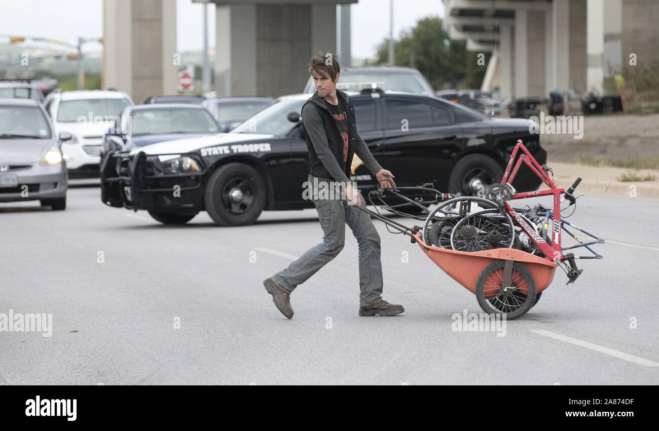 November 6, 2019: Michael Cavazos hauls belongings across the highway blocked by a state trooper during the third day of a state-sanctioned homeless camping crackdown in Texas' capital city. On orders from Texas Gov. Greg Abbott, highway crews are clearing 17 identified homeless camps on major highways. Credit: Bob Daemmrich/ZUMA Wire/Alamy Live News Stock Photo