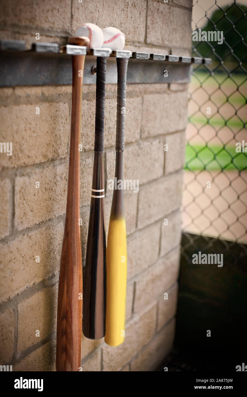 Three baseball bats hanging from a wall rack below two baseballs Stock