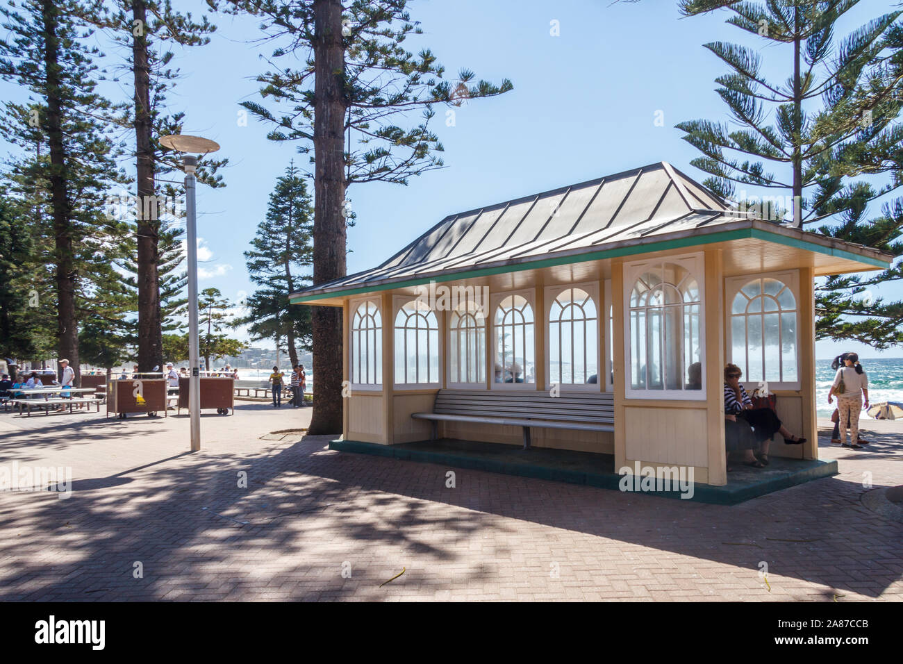 Manly, Australia - March 13th 2013: People resting in a shelter on the promenade. The shelter was erected in 1940 Stock Photo