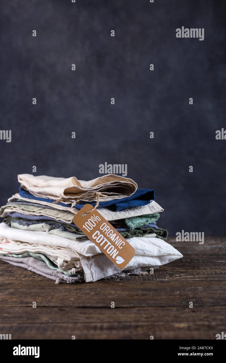Pile of things lie on a wooden table. Cotton, linen items in pastel colors shirts, shreds of fabric, shawls. Stock Photo