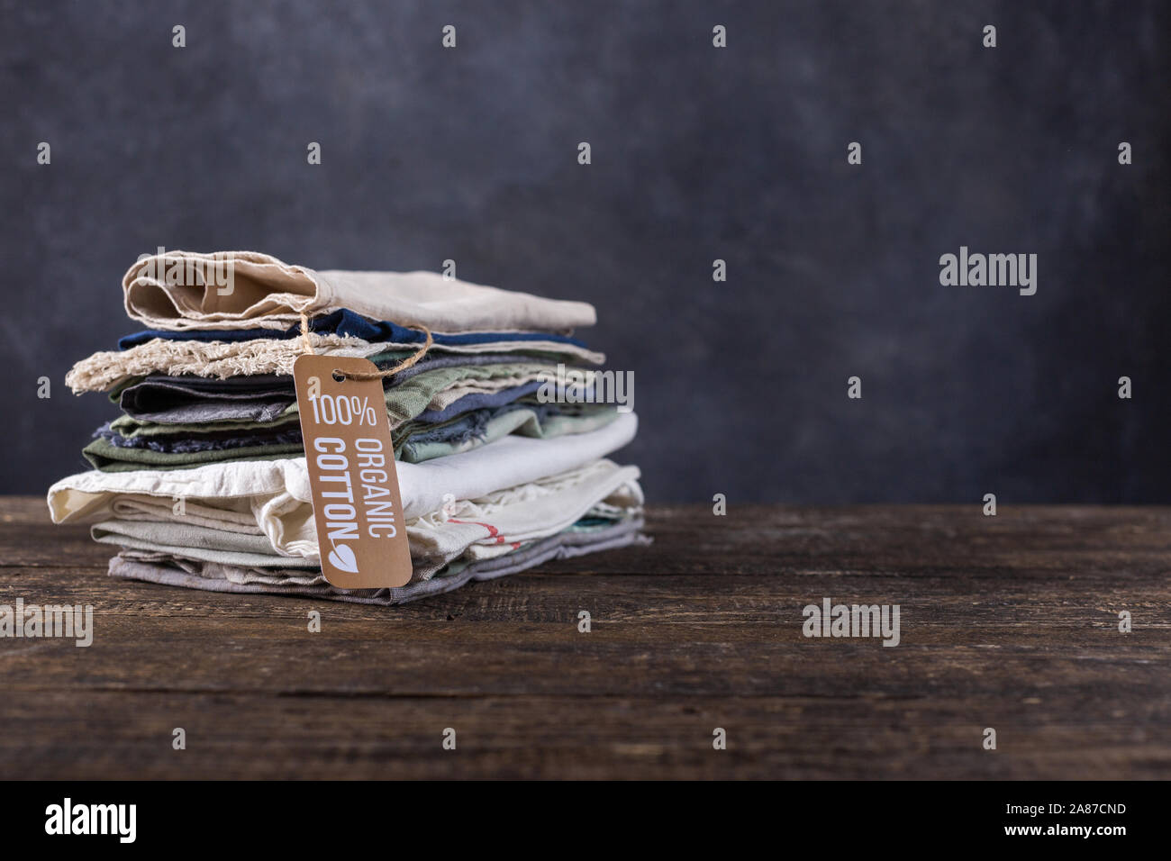 Pile of things lie on a wooden table. Cotton, linen items in pastel colors shirts, shreds of fabric, shawls. Stock Photo