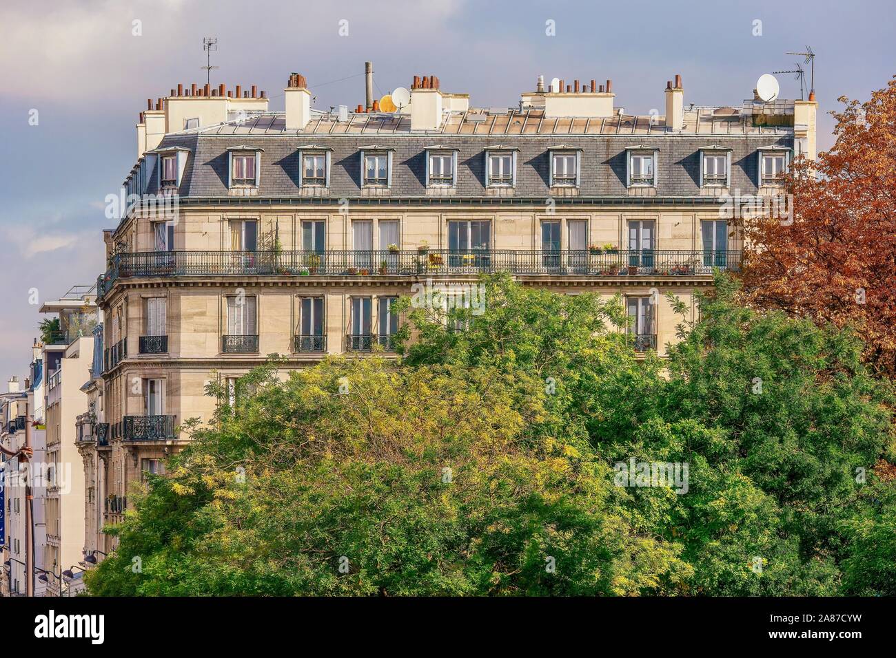 A traditional Parisian apartment building in a residential neighborhood, with large trees adding nature to the urban setting. Stock Photo