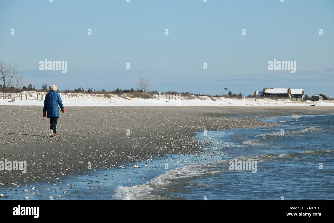 Old Lyme, CT / USA - March 3, 2019: Lone woman walking along the shore and getting some exercise despite the chill Stock Photo