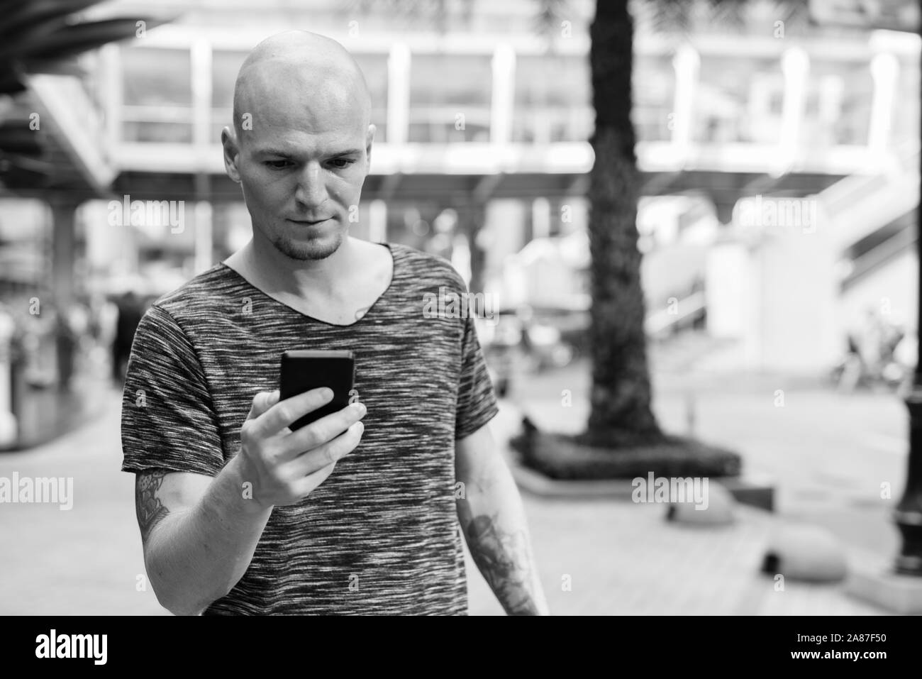 Young handsome bald man using mobile phone outside the mall Stock Photo