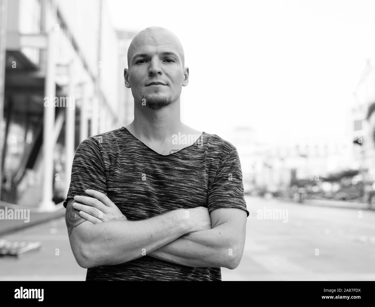 Young handsome bald man with arms crossed outside of the mall in the city Stock Photo